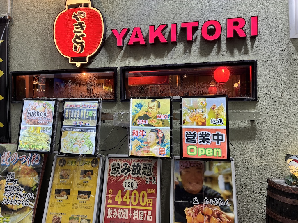 Yakitori izakaya storefront with all-you-can-drink offer in a Naha shopping street at night
