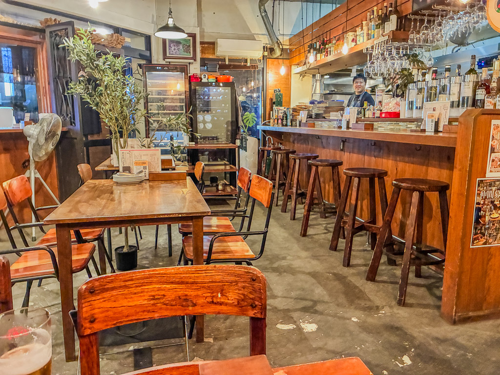 ALGOS DELI×HAMBURG interior — wooden counter and open kitchen lined with wine bottles