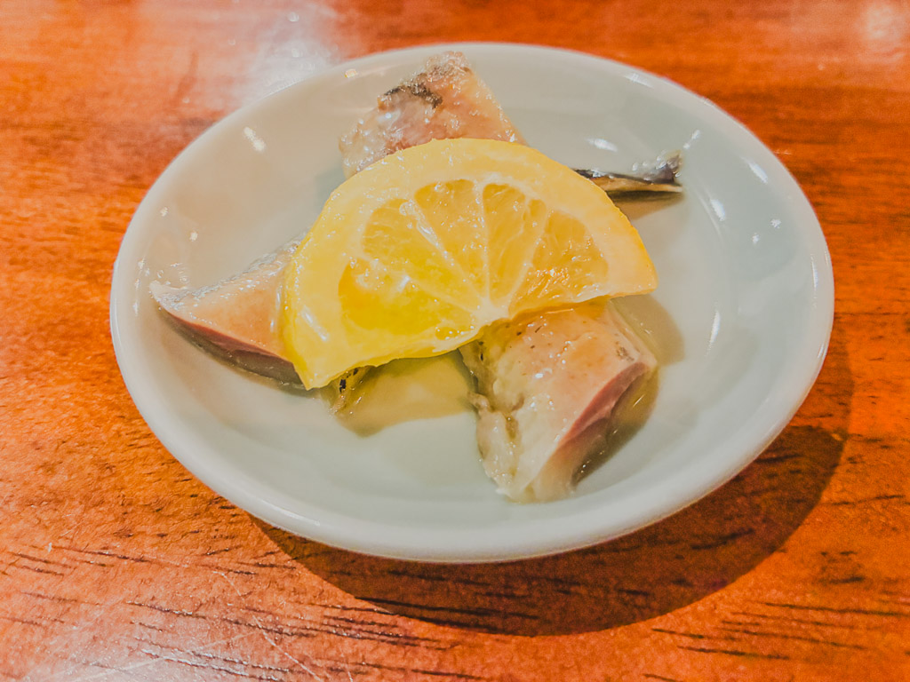 ALGOS DELI×HAMBURG otoshi — small plate of lightly cooked white fish with a lemon slice