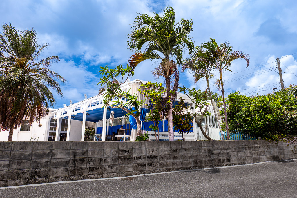 港川 (Minatogawa) palm trees with white buildings and blue canopy, tropical vibe — Okinawa Urasoe Stateside town street