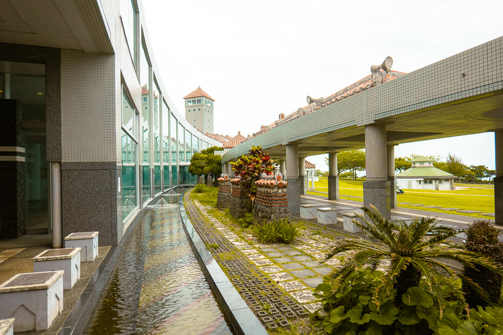 Museum colonnade with reflecting water pool — Ryukyu red tiles and Peace Memorial Hall tower in view