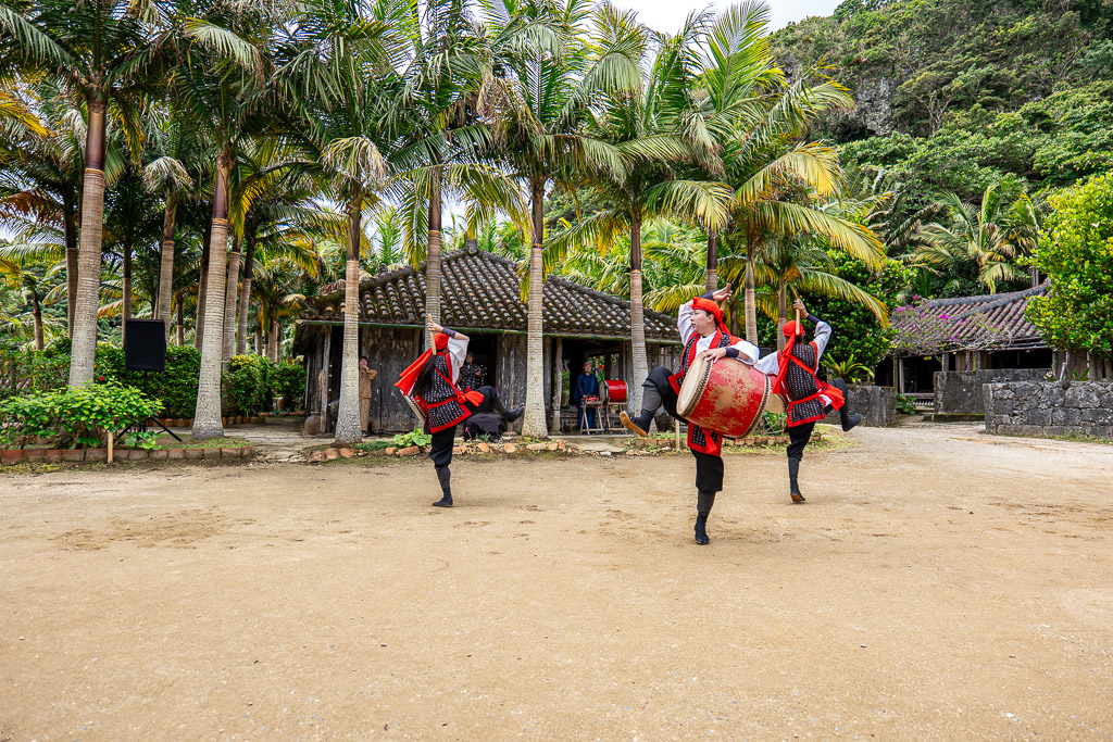 Wide shot of Eisa drum performance with three drummers and audience watching the central plaza show
