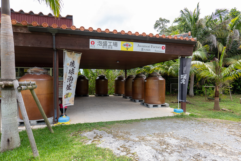 Sakimoto Sake Brewery entrance with seven massive reddish-brown Awamori jars lined up and Ryukyu Awamori banner