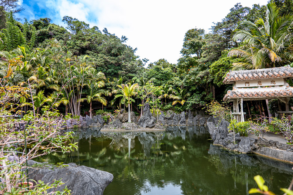 Spring-water pond inside Ryukyu Village with greenery reflected on the surface and small red-tile gazebo