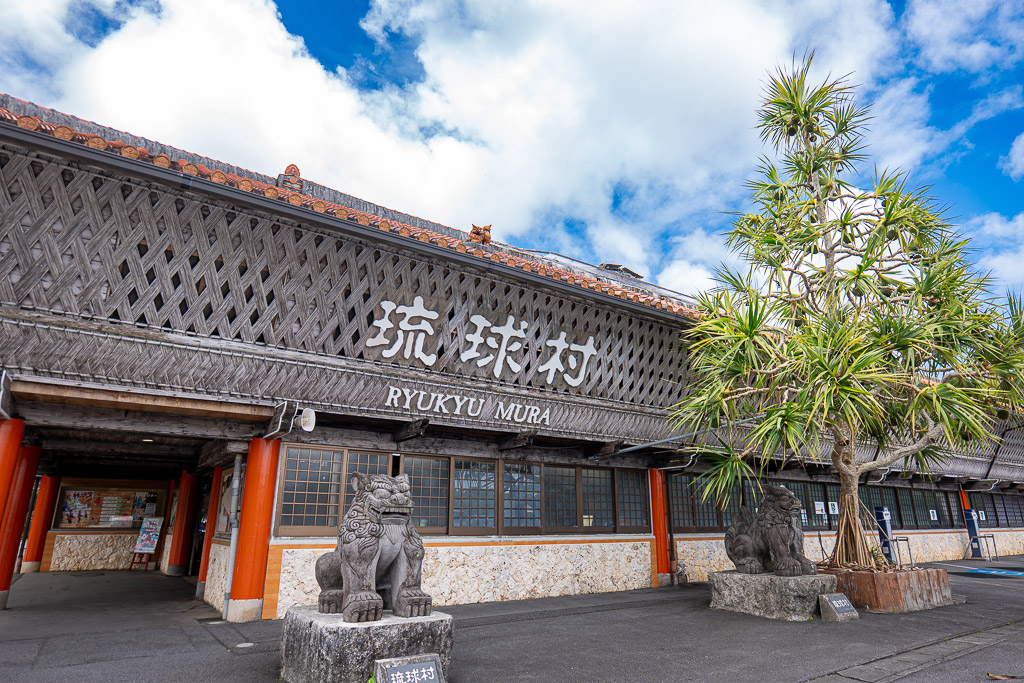 Full view of Ryukyu Village main gate with woven-style large roof and two Shisa lion-dogs guarding the Ryukyu Village signboard
