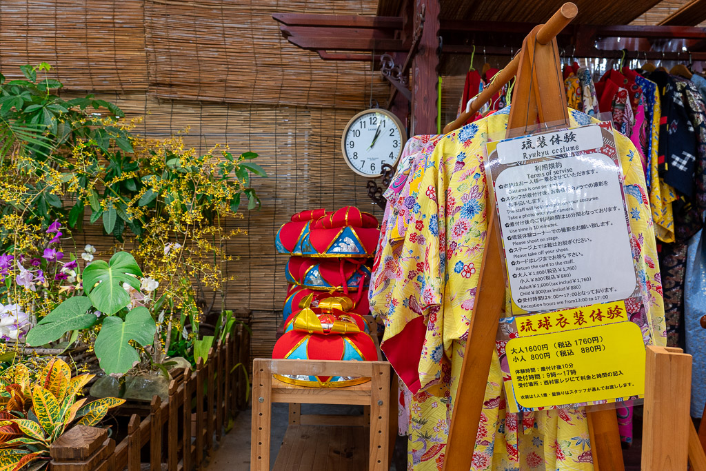 Ryukyu costume experience corner at Bios no Oka — yellow and red traditional Ryukyu outfits hanging on a wooden rack