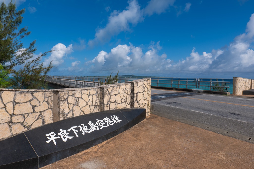 Irabu Ohashi Bridge entrance monument with turquoise sea and the bridge stretching out behind