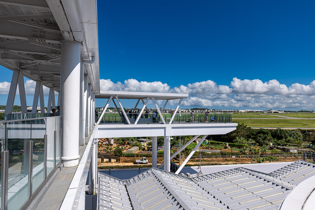 Rooftop observation deck at Michi-no-Eki Kadena with visitors looking out over Kadena Air Base under a bright blue sky