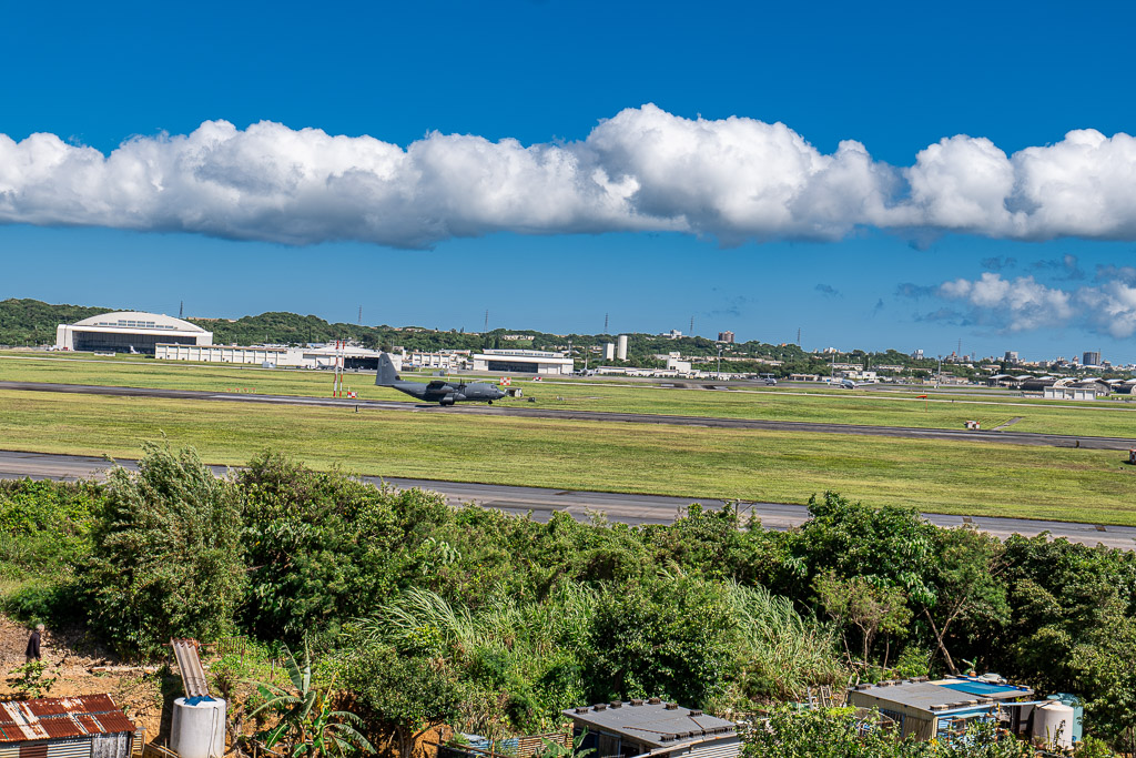 C-130 turboprop moving along the runway with hangars in the background at Kadena