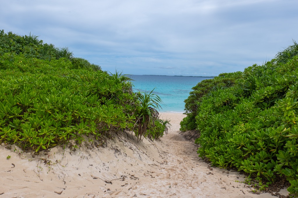 Sand path between dunes opening to a glimpse of turquoise sea at Sunayama Beach