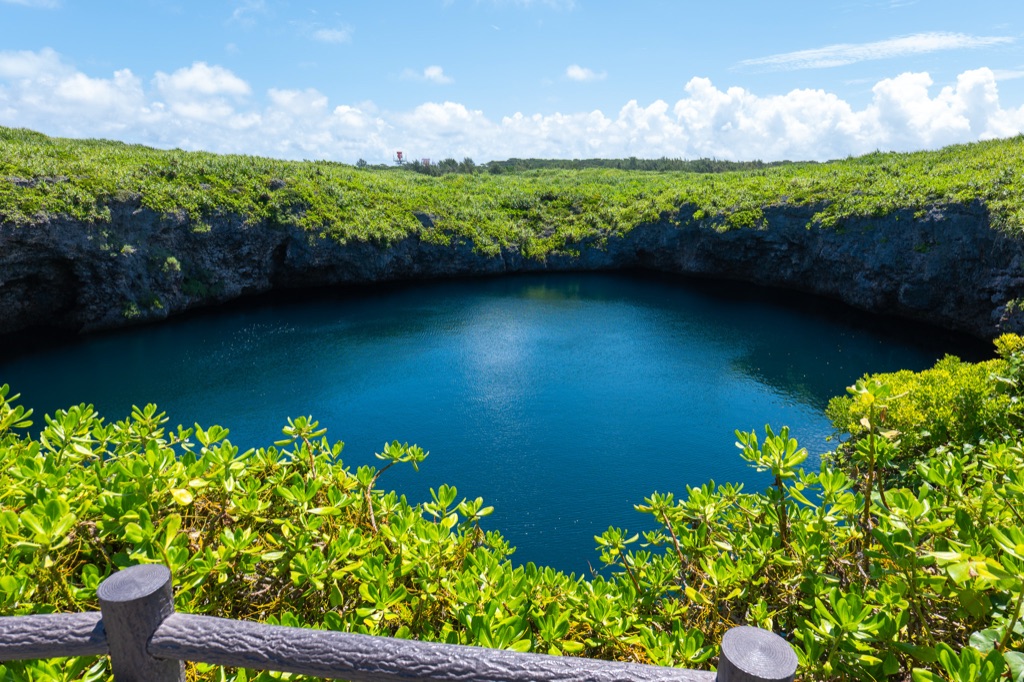 Large inland sinkhole at Toriike Pond Miyakojima with deep sapphire water ringed by green cliffs