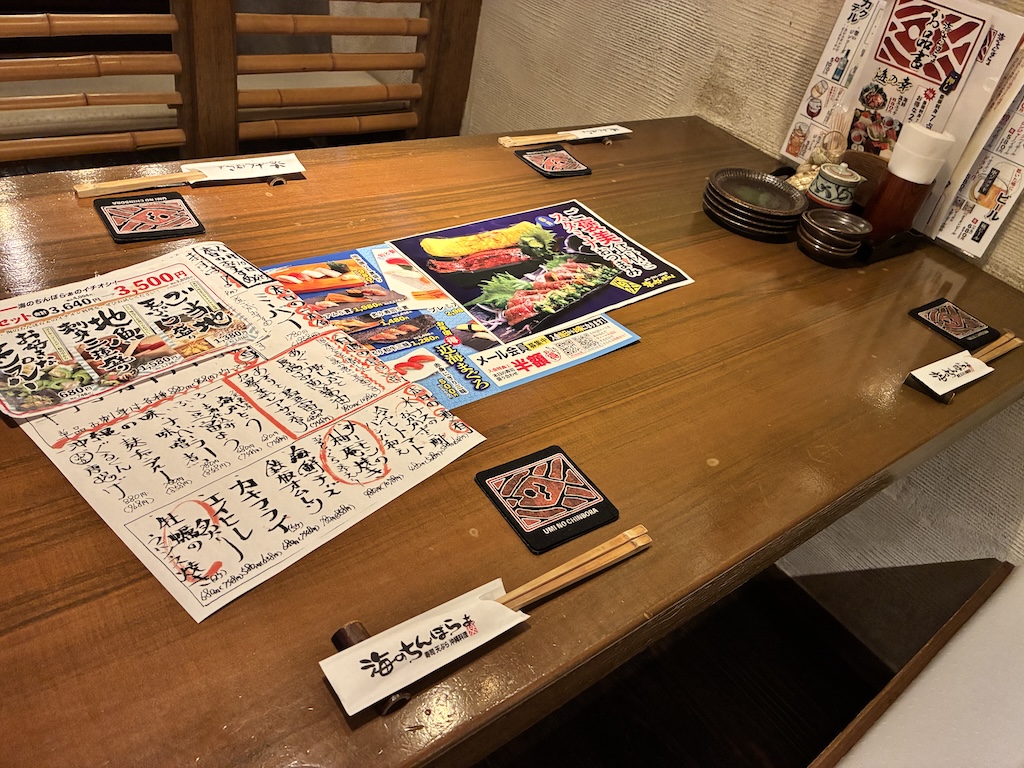 Wooden izakaya table with menus and chopsticks branded with the Umi no Chinbora logo