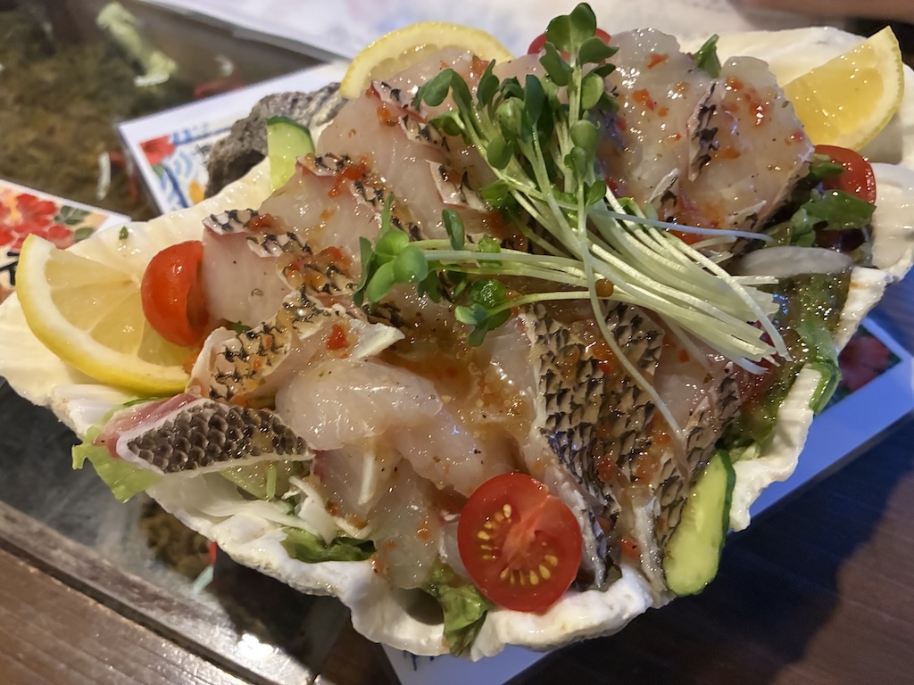 A sea bream carpaccio plate with cherry tomatoes, lemon wedges, and microgreens at a Japanese izakaya