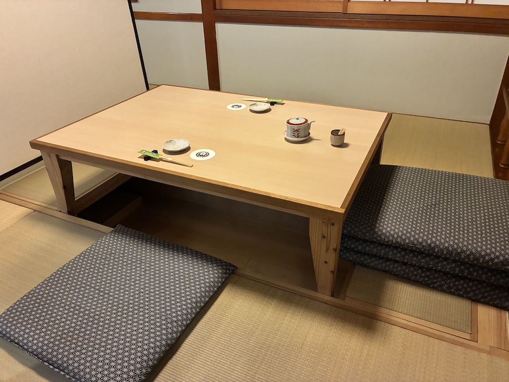 A traditional Japanese tatami room with a low wooden zashiki table, cushions, and a small teapot — classic restaurant interior