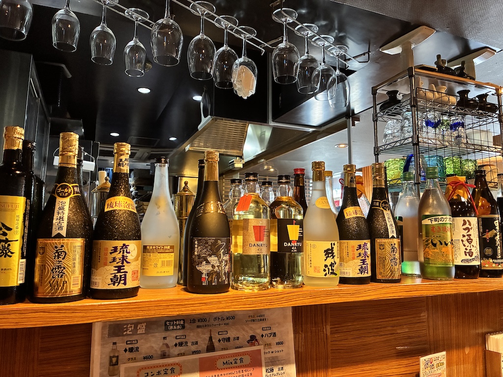 A shelf of Japanese sake, awamori, and shochu bottles at an Osaka izakaya bar
