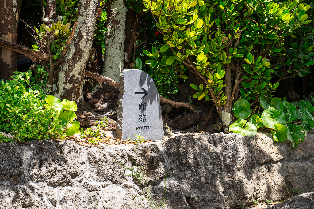 Stone marker with an arrow and the word ROUTE guiding walkers along the Bise Fukugi Tree Road path