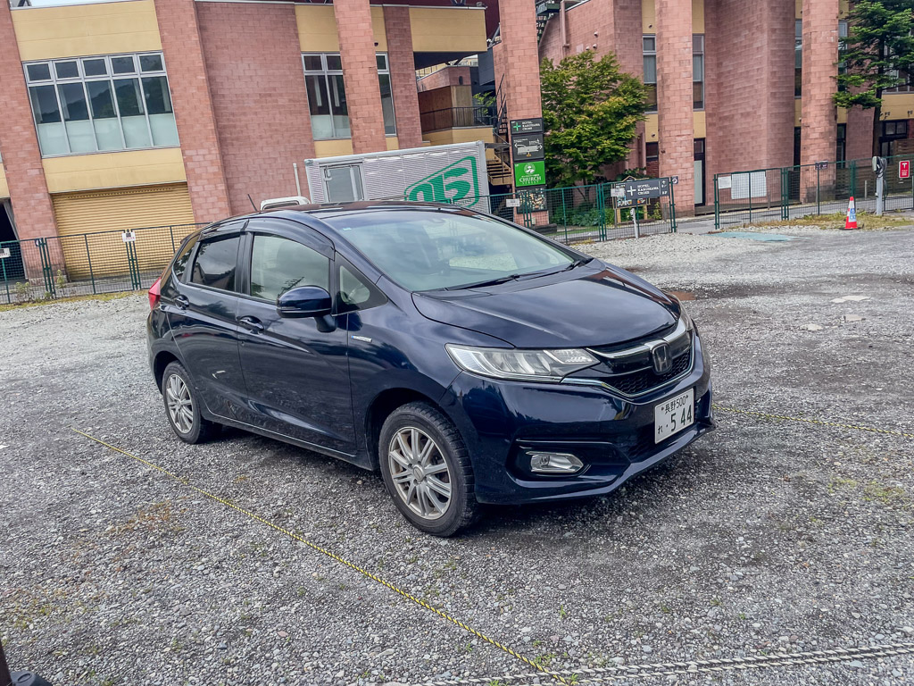 Nagano rental car: navy Honda FIT hybrid parked in front of a brick building in Karuizawa