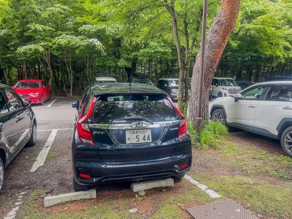 Nagano rental car rear view of the Honda FIT hybrid parked at a leafy Karuizawa lot