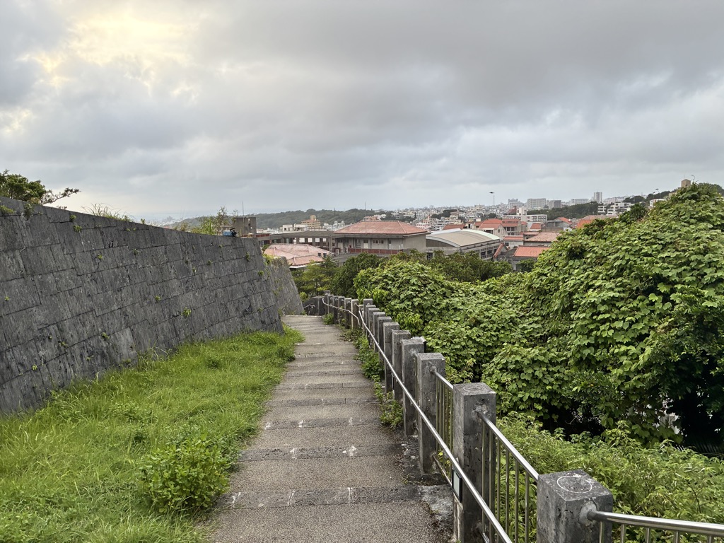 Stone rampart and a downhill stairway with Naha rooftops in the distance