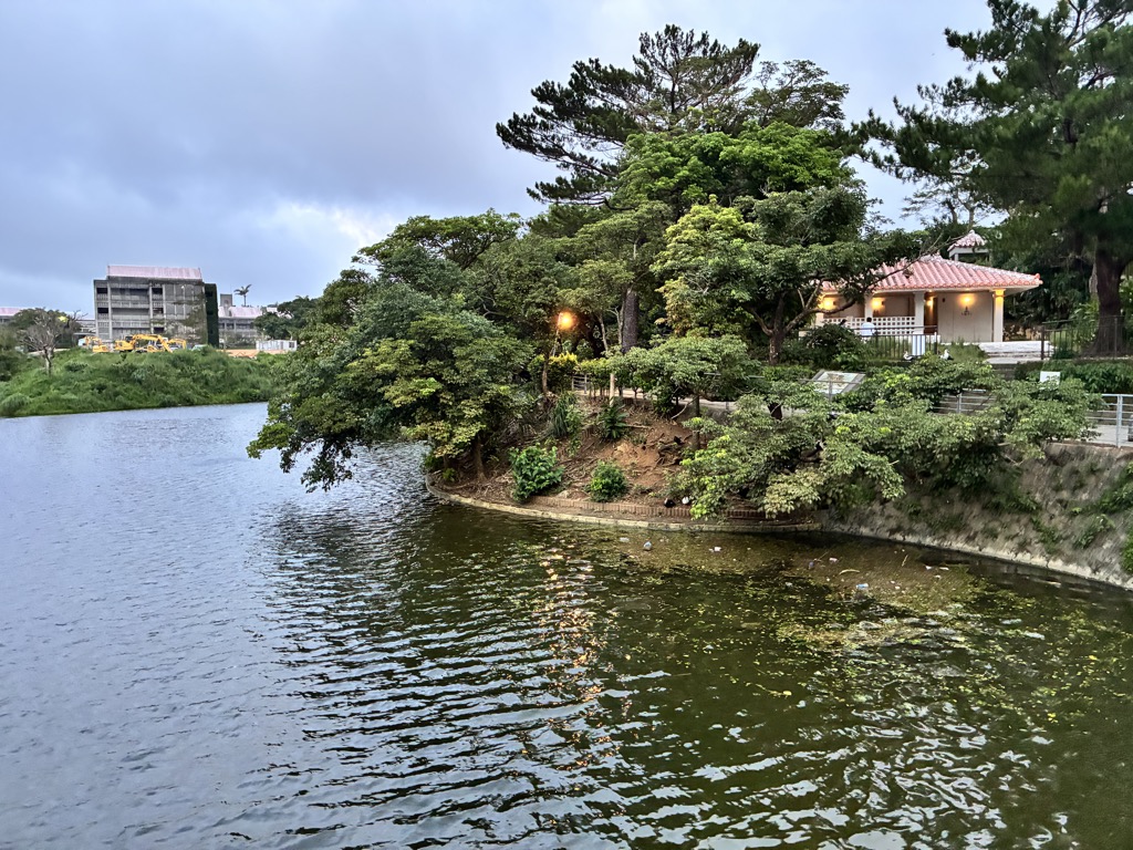 Illuminated red-tiled hall reflected in a Shuri Castle Park pond at dusk with a crane behind