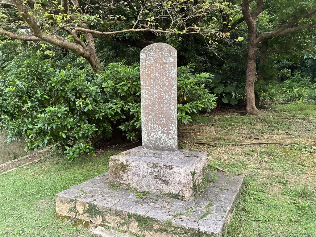 Weathered old stone monument standing among trees in Shuri Castle Park