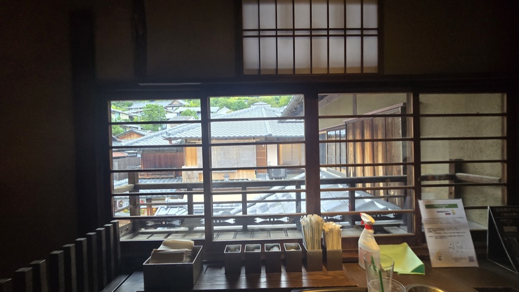 Traditional wooden machiya interior with latticework windows framing a view of tiled Kyoto rooftops from a Ninenzaka café