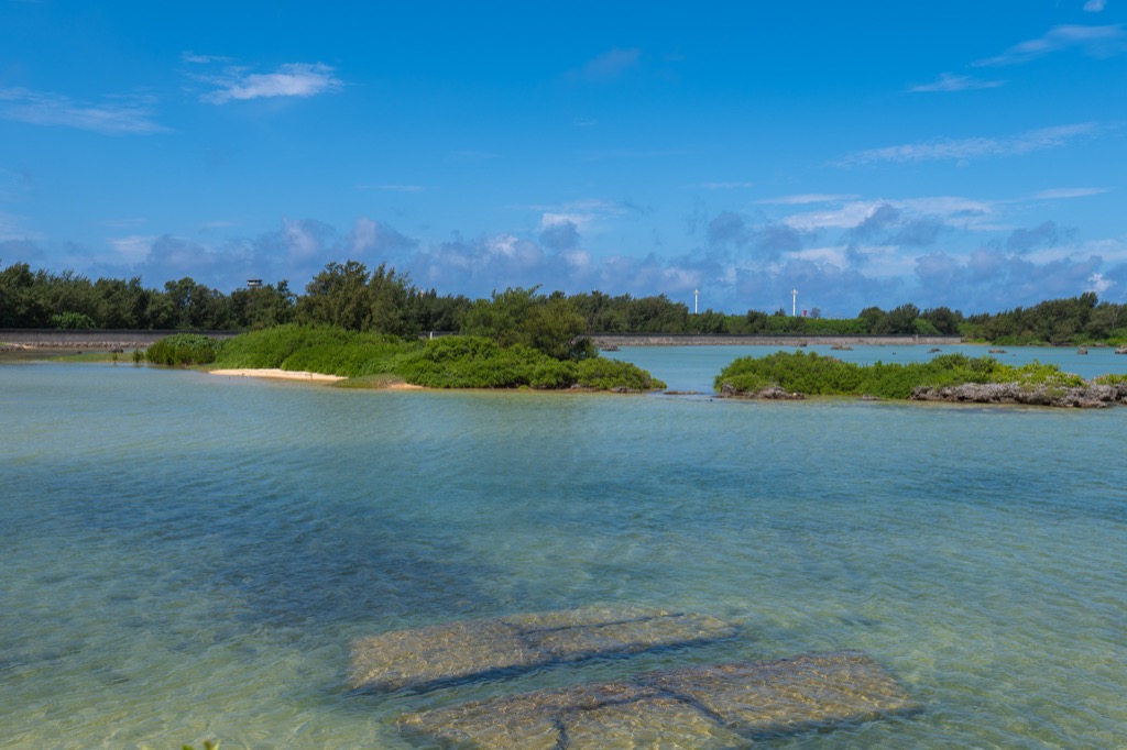 Small green islet floating in the shallow flats of Sawada-no-hama with distant Irabu observatory tower
