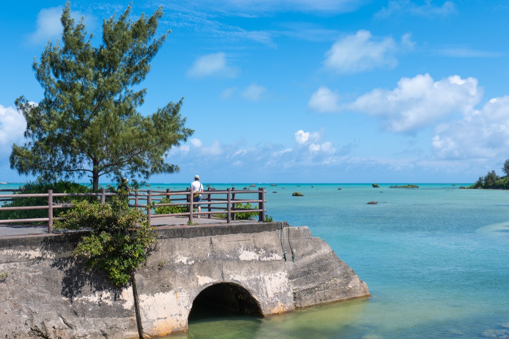 A visitor standing on a short concrete pier at Sawada-no-hama looking out over turquoise water