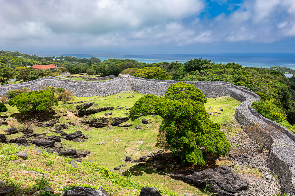 Sweeping curved stone walls of Nakijin Castle Ruins overlooking green forest and blue sea in Northern Okinawa