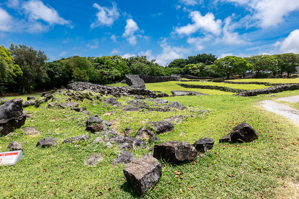 Green grassy field with scattered stone ruins inside Nakijin Castle Ruins under blue sky