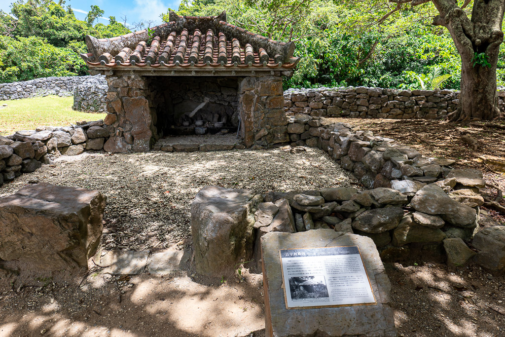 Small stone shrine with a red-tiled roof set among the trees inside Nakijin Castle Ruins