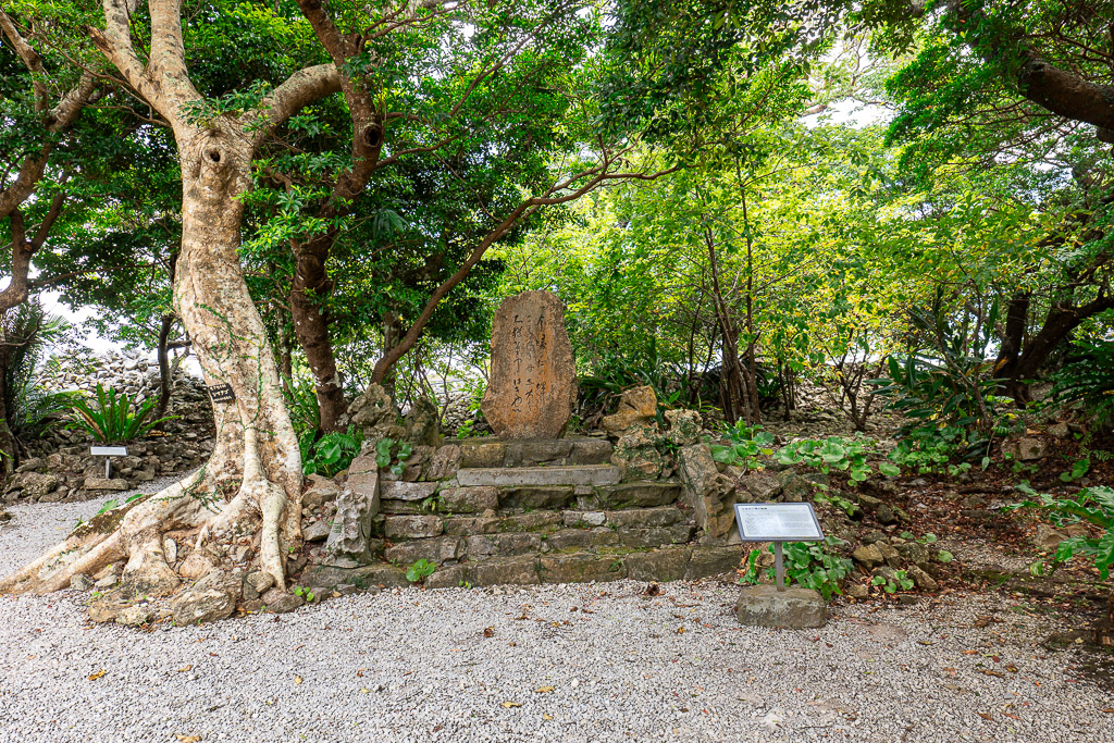 Old weathered stone stele on a stairway shaded by tropical trees inside Nakijin Castle Ruins