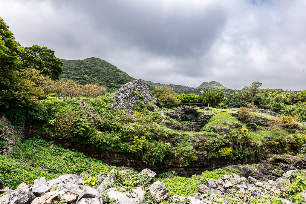 Broken castle wall rubble at Nakijin Castle Ruins with green vegetation reclaiming the stones