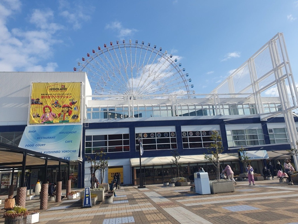 Early December daytime scene at Tempozan Marketplace plaza in Osaka, visitors in coats under a clear winter-blue sky