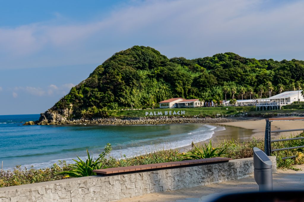 Palm Beach sign and the Itoshima coastline just west of Meoto Iwa — the cafe-and-resort strip right beside the rocks