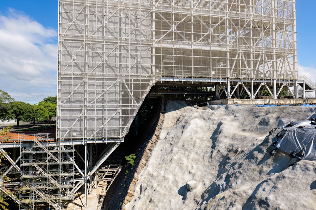 Stone-wall repair site with numbered pieces laid out below scaffolding