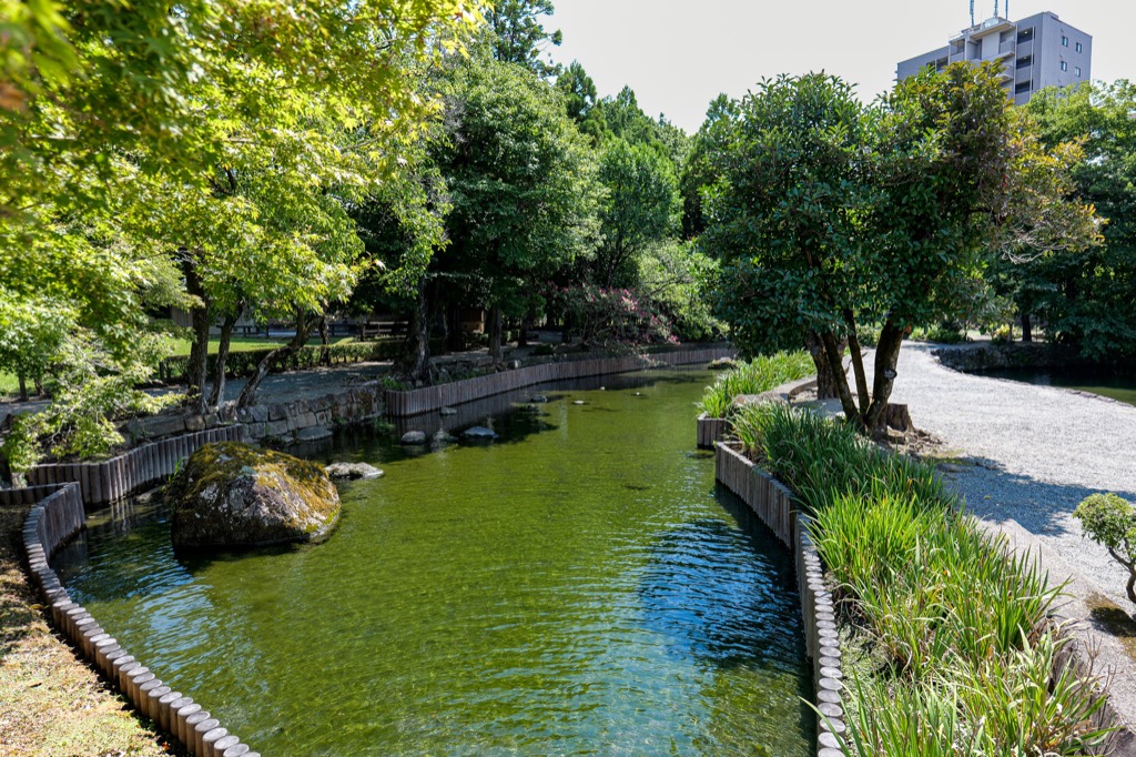 Narrow waterway and shaded path inside Suizenji Jojuen Garden