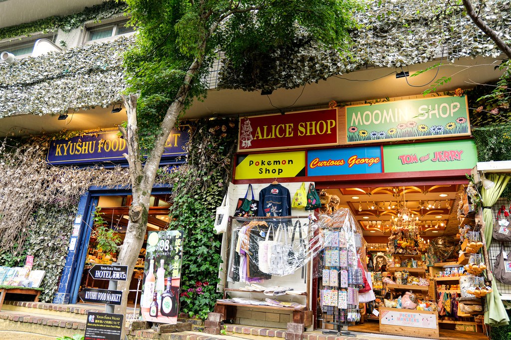 Floral Village character shop lineup with Kyushu Food Market, Alice Shop, Pokemon Shop, Curious George, Tom and Jerry and Moomin Shop signs